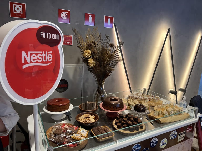 Mesa cheia de doces e sobremesas, como bolos de chocolate e brownies, todos preparados com os produtos Nestlé. À esquerda da