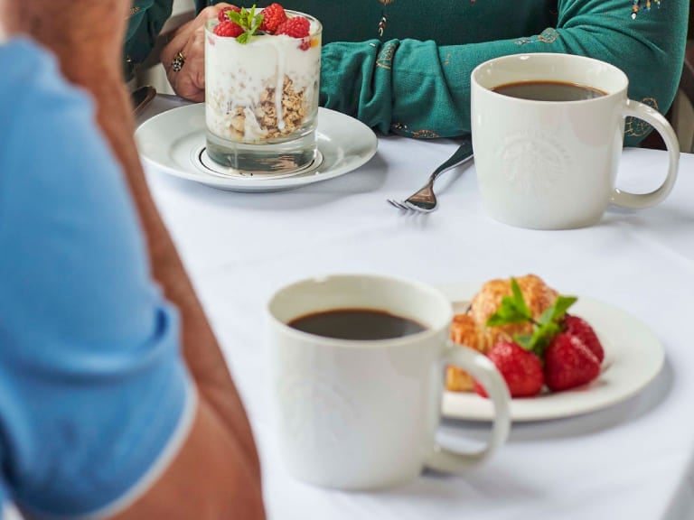 Foto de uma mesa de café da manhã de hotel, com xícaras de café e frutas como morango