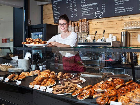 Atendente de cafeteria mostra doces e salgados que estão na vitrine, como croissants e cookies – Ideias para Páscoa 2024.