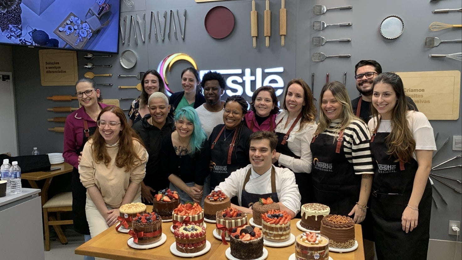 Grupo de chefs confeiteiros e influenciadores digitais posam para foto. Em destaque na imagem, há diversos bolos preparados.