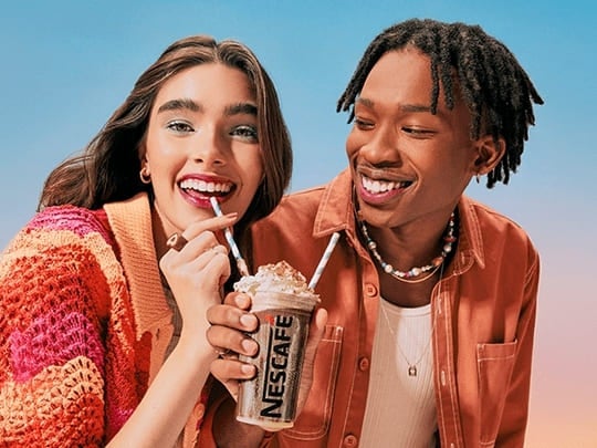 Mulher (à esquerda) e homem sorriem enquanto dividem copo de bebida nescafé gelado com dois canudos