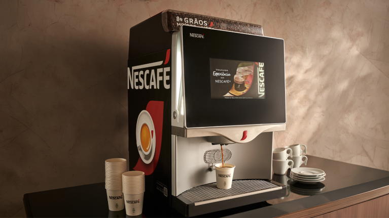 Máquina de café Nescafé servindo espresso; copos e xícaras ao lado.