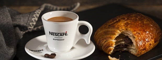 Delicioso café Nescafé, servido em pires e xícara brancas Nescafé com um croissant de chocolate