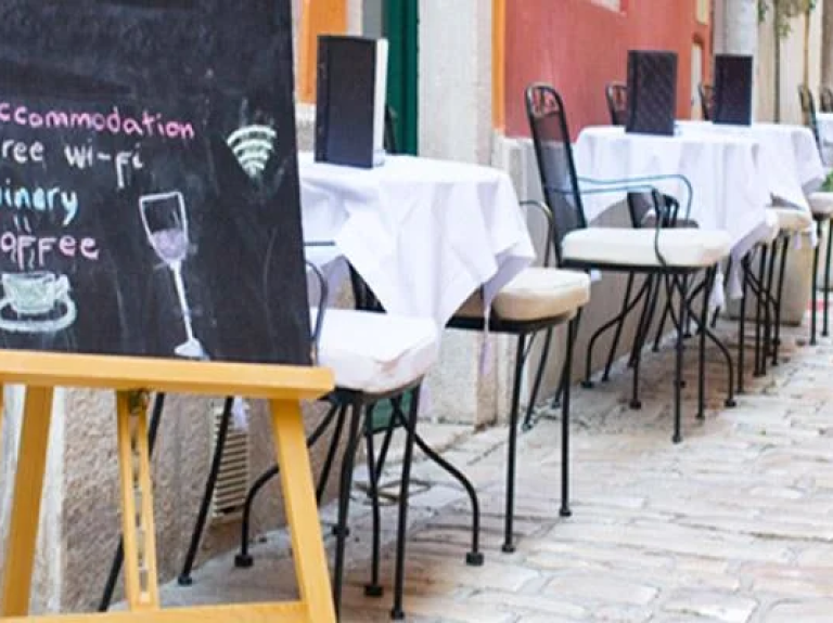 Foto de mesas de restaurante, com cardápios abertos e um letreiro na porta