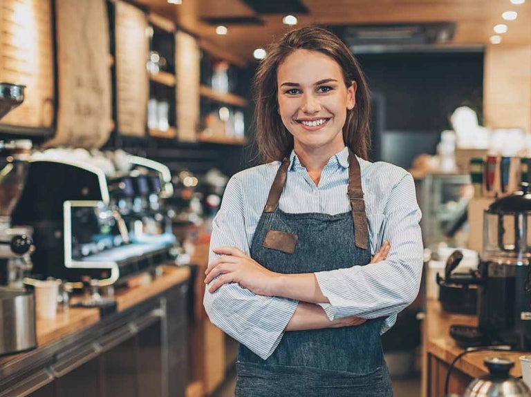 Mulher barista de braços cruzados sorri em cafeteria