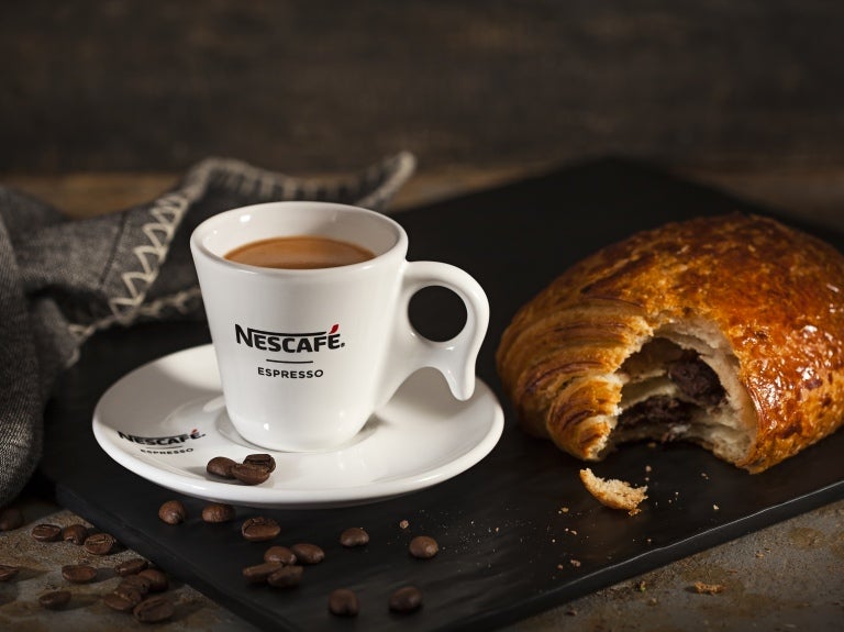 Delicioso café Nescafé, servido em pires e xícara brancas Nescafé com um croissant de chocolate