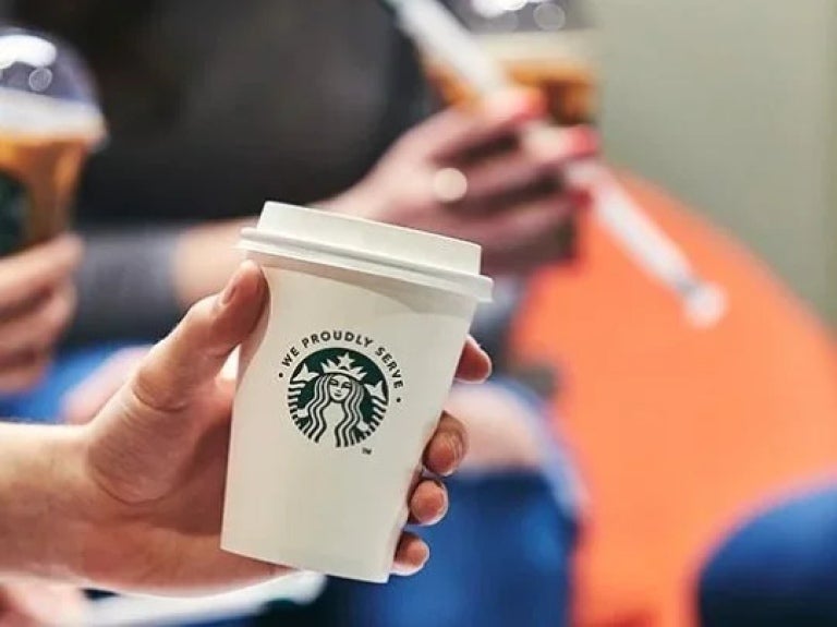 Copo de material reciclável com o logo da starbucks sendo segurado por um homem