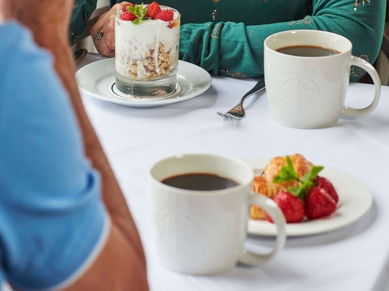 Foto de uma mesa de café da manhã de hotel, com xícaras de café e frutas como morango