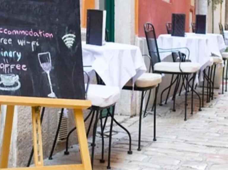 Foto de mesas de restaurante, com cardápios abertos e um letreiro na porta