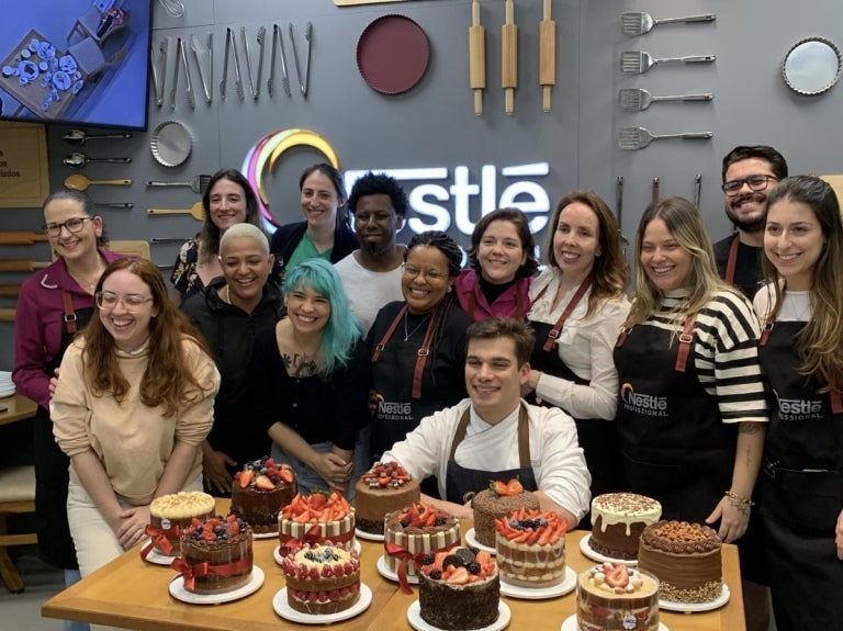 Grupo de chefs confeiteiros e influenciadores digitais posam para foto. Em destaque na imagem, há diversos bolos preparados.