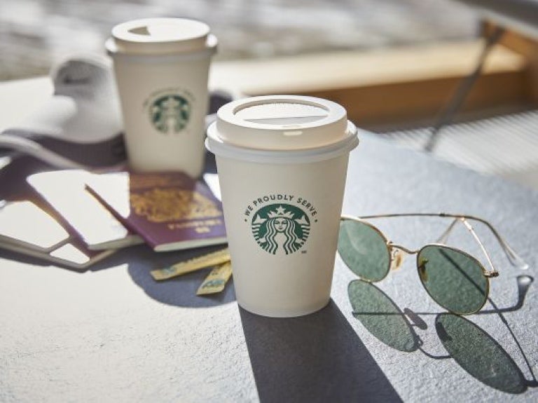 Mesa externa de uma cafeteria contendo passaportes, produtos starbucks e um óculos de sol