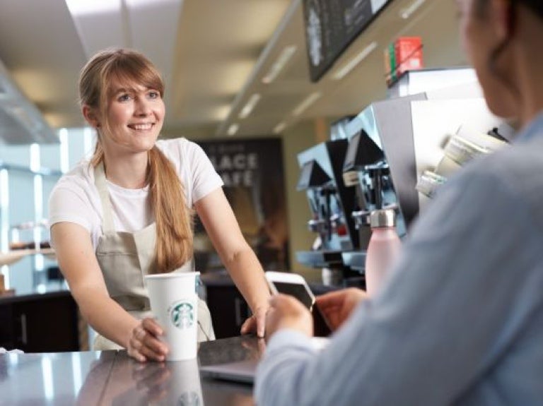 Mulher profissional em uma cafeteria entregando um produto starbucks para cliente