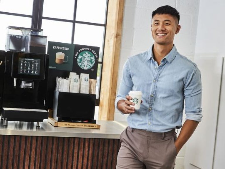 Cliente feliz segurando sua bebida starbukcs ao lado de uma ma´quina profissional de café
