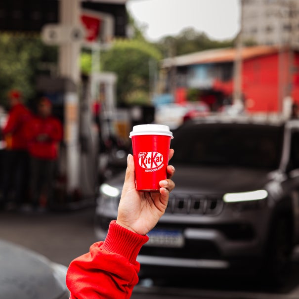 Mão segura copo térmico vermelho da marca KitKat em um posto de gasolina - Nestlé Professional