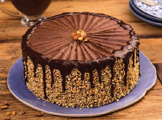 Bolo de chocolate decorado com pedaços de amendoim ao seu redor e na cobertura - Charge chocolate