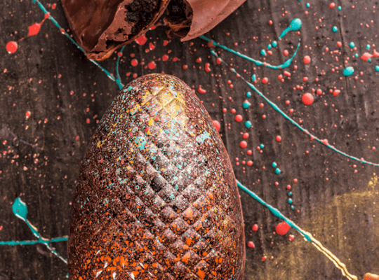 Ovo de Páscoa de chocolate é brilhante e tem detalhes coloridos com diversos respingos em cores azul, amarelo e vermelho