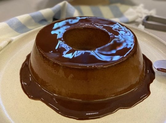 Imagem mostra um pudim de chocolate feito com Alpino, que transborda uma calda de chocolate pelo prato; é um pudim de formato