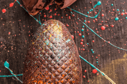 Ovo de Páscoa de chocolate é brilhante e tem detalhes coloridos com diversos respingos em cores azul, amarelo e vermelho