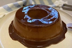 Imagem mostra um pudim de chocolate feito com Alpino, que transborda uma calda de chocolate pelo prato; é um pudim de formato
