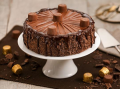Bolo de chocolate coberto com bombons Alpino, está sob um prato branco, apoiado em uma mesa que tem mais bombons Alpino espal