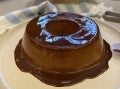 Imagem mostra um pudim de chocolate feito com Alpino, que transborda uma calda de chocolate pelo prato; é um pudim de formato