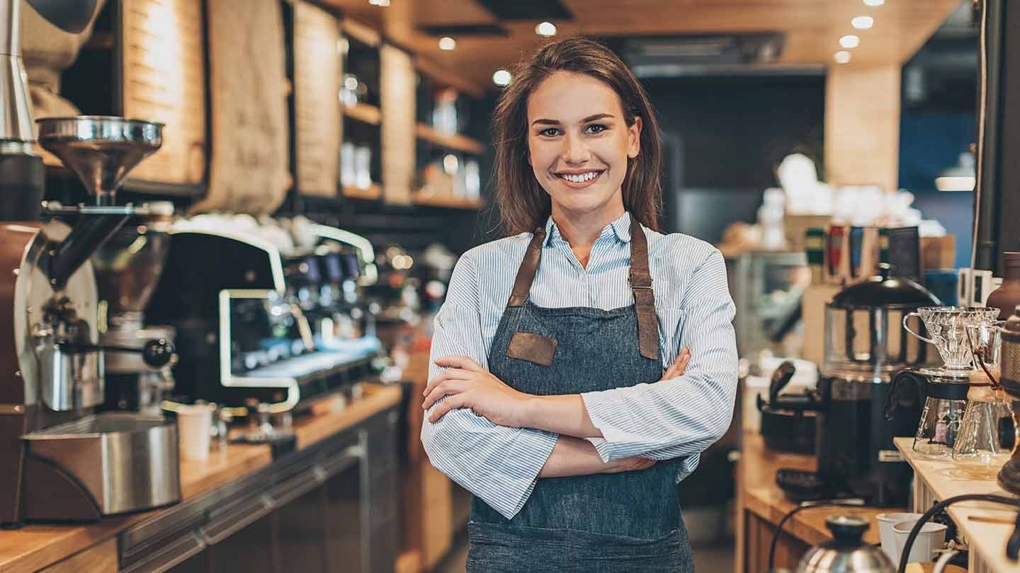 Mulher barista de braços cruzados sorri em cafeteria