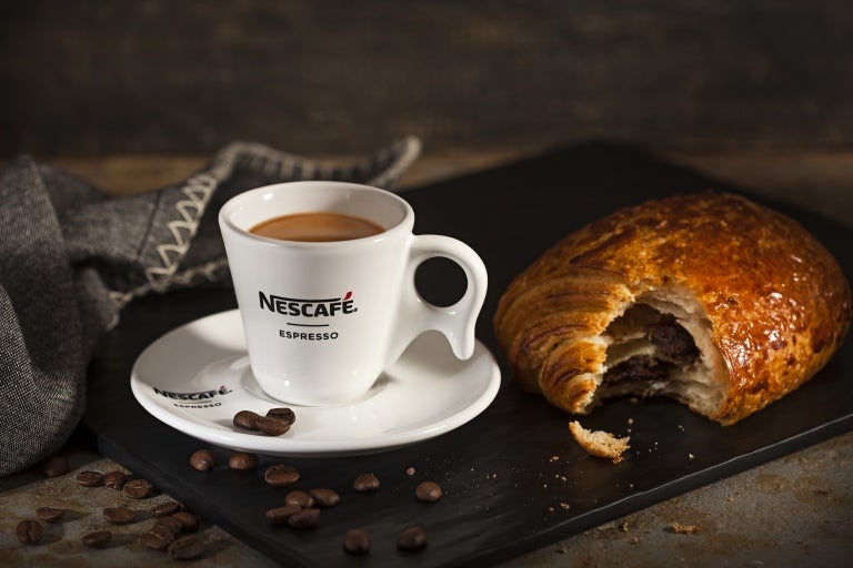 Delicioso café Nescafé, servido em pires e xícara brancas Nescafé com um croissant de chocolate