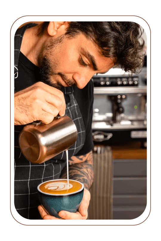 Barista utilizando um bule com leite para desenhar no café que está na xicara